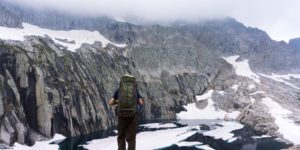 man with backpack on top of cliff staring at mountain